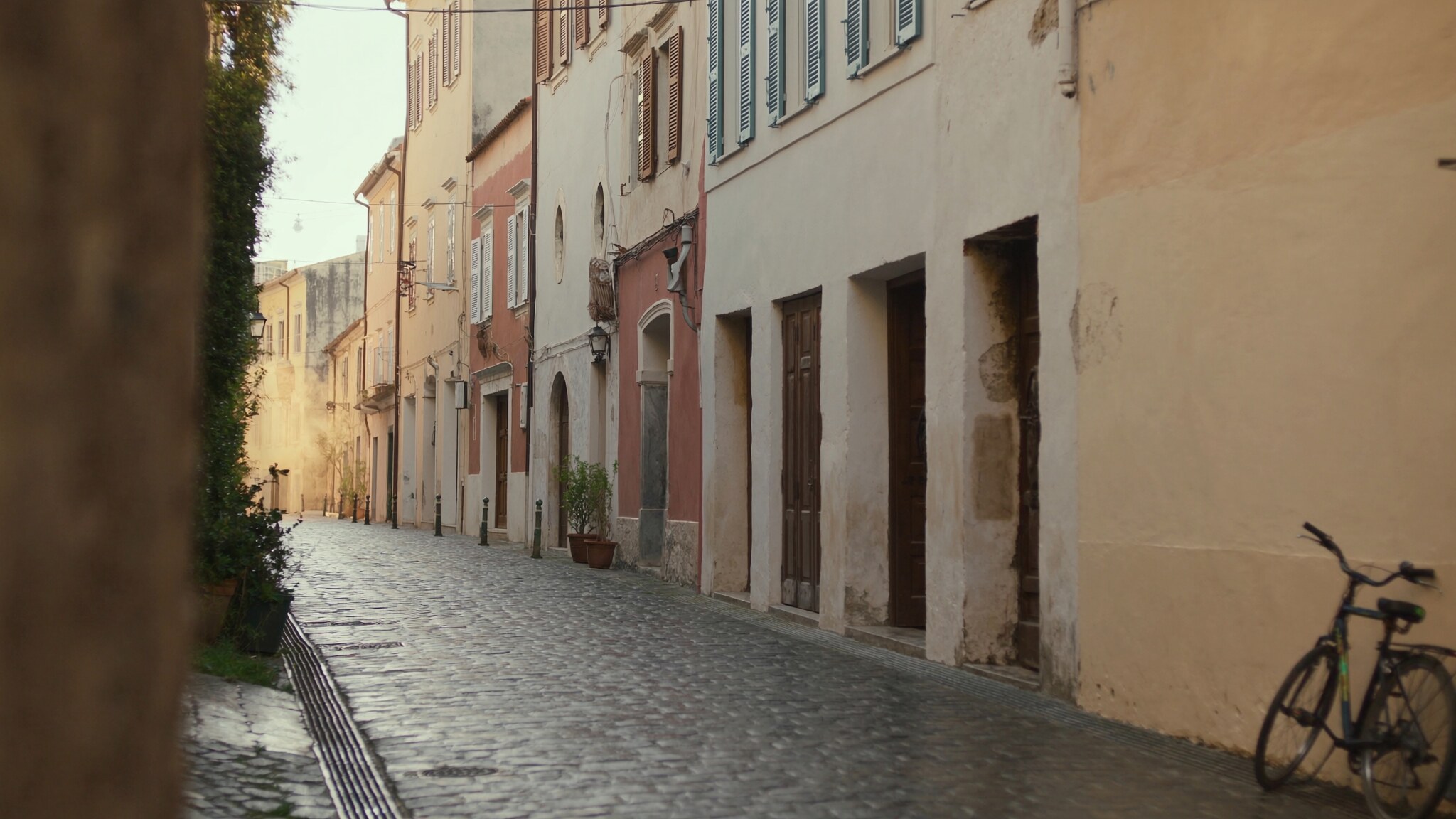 A quiet old city street after rain with stone paving, shuttered buildings, and morning light.